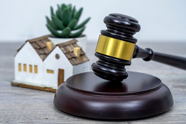 A háttérben egy ház kicsinyített máse, az előtérben egy fa korong rajta egy kalapács